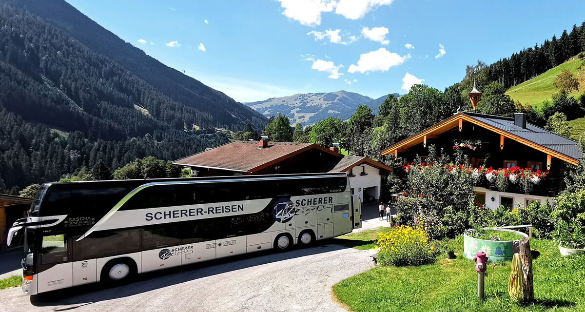 Seitenansicht von Saschas silbernem Doppeldeckerbus vor einer großen Hütte inmitten der Berge.
