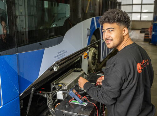 Mann arbeitet an der Technik eines Scherer-Reisen Linienbusses in einer Werkstatt und blickt lächelnd in die Kamera.