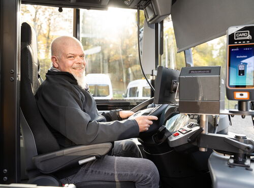 Scherer-Reisen Busfahrer sitzt am Steuer, hält das Lenkrad und lächelt in die Kamera.