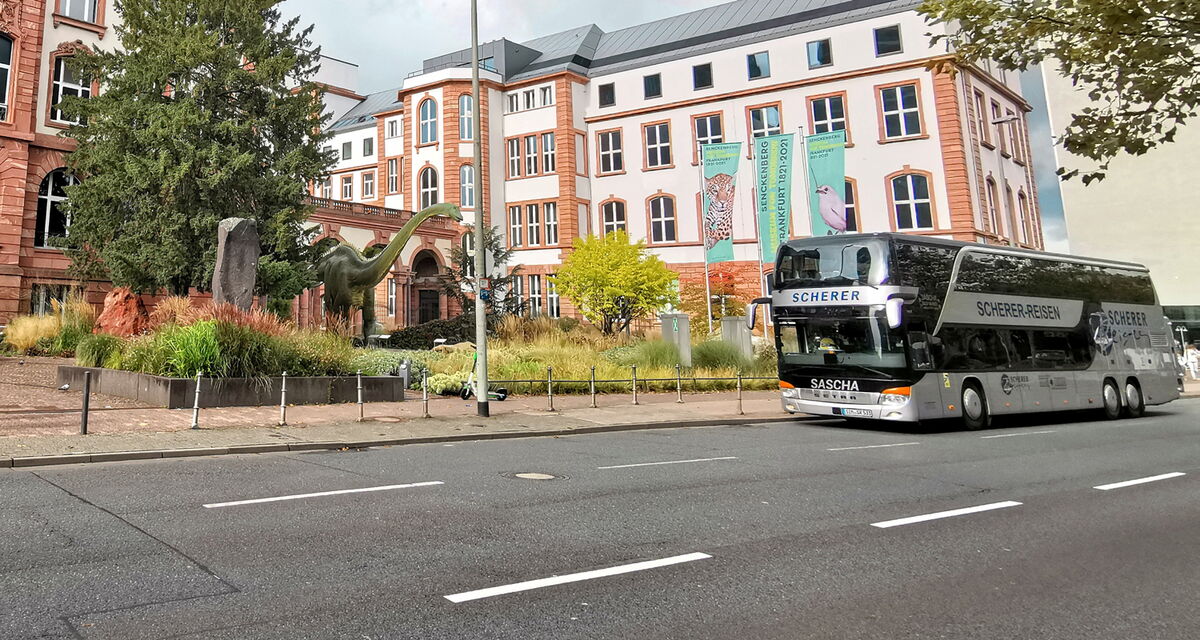 Saschas silberner Doppeldeckerbus vor dem Senckenberg Naturmuseum in Frankfurt am Main mit Dinosaurierstatue im Vorhof.