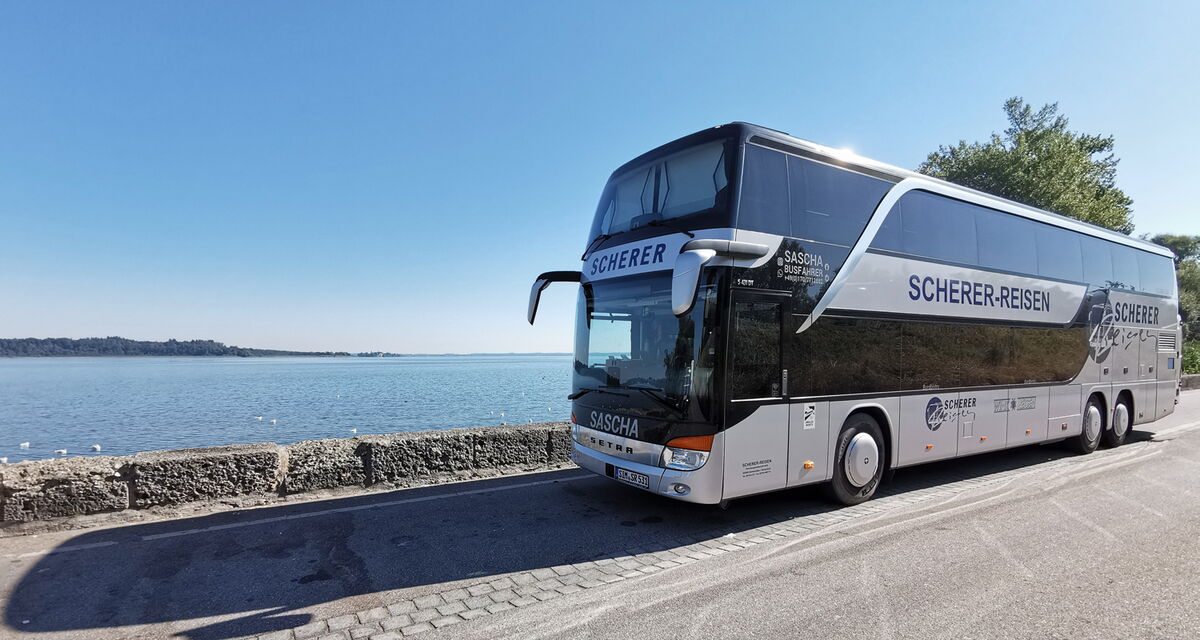 Saschas silberner Doppeldeckerbus direkt am Meer bei blauem Himmel.