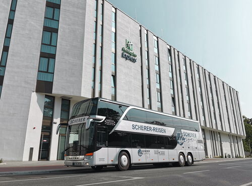 Saschas silberner Doppeldeckerbus steht vor dem Gebäude „Holiday Inn Express“.