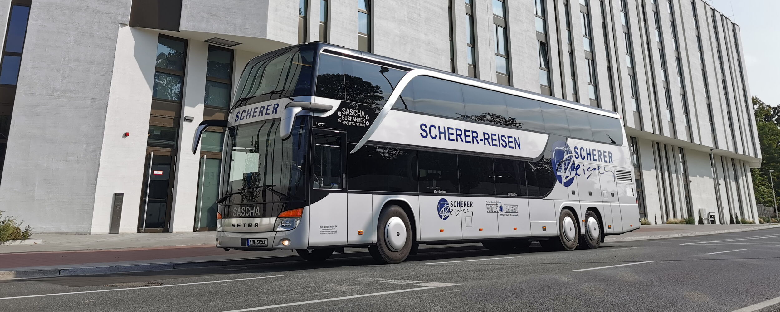 Saschas silberner Doppeldeckerbus vor dem Gebäude „Holiday Inn Express“.