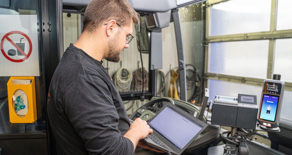 Mann prüft am Laptop die Technik eines Scherer-Reisen Busses und steht am Bezahlungsgerät.