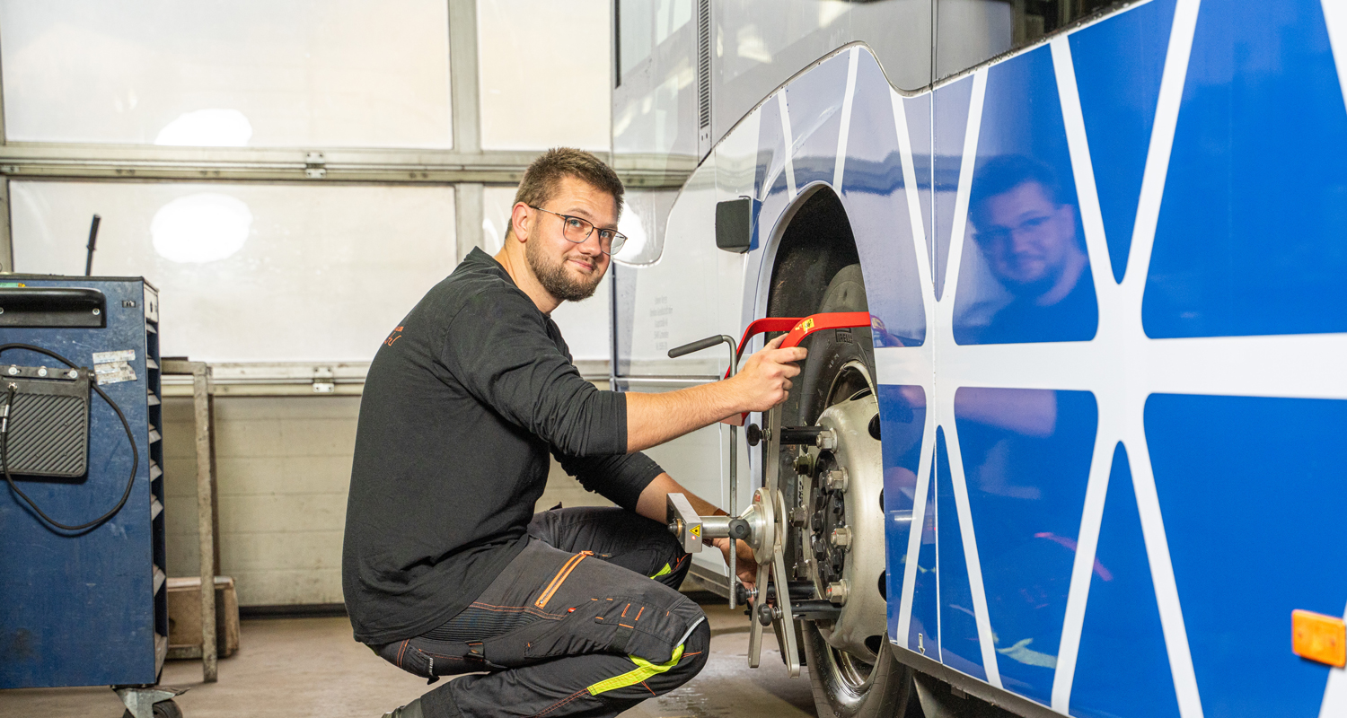 Mann arbeitet an dem Rad eines Scherer-Reisen Linienbusses und schaut in die Kamera.