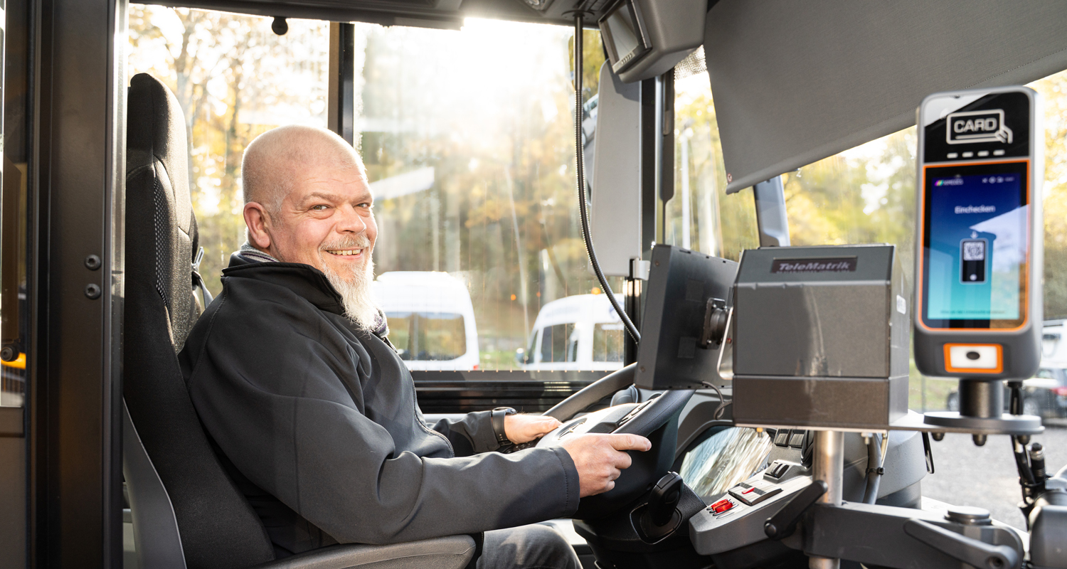 Busfahrer sitzt am Steuer eines Scherer-Reisen Busses, hält das Lenkrad und lächelt in die Kamera.