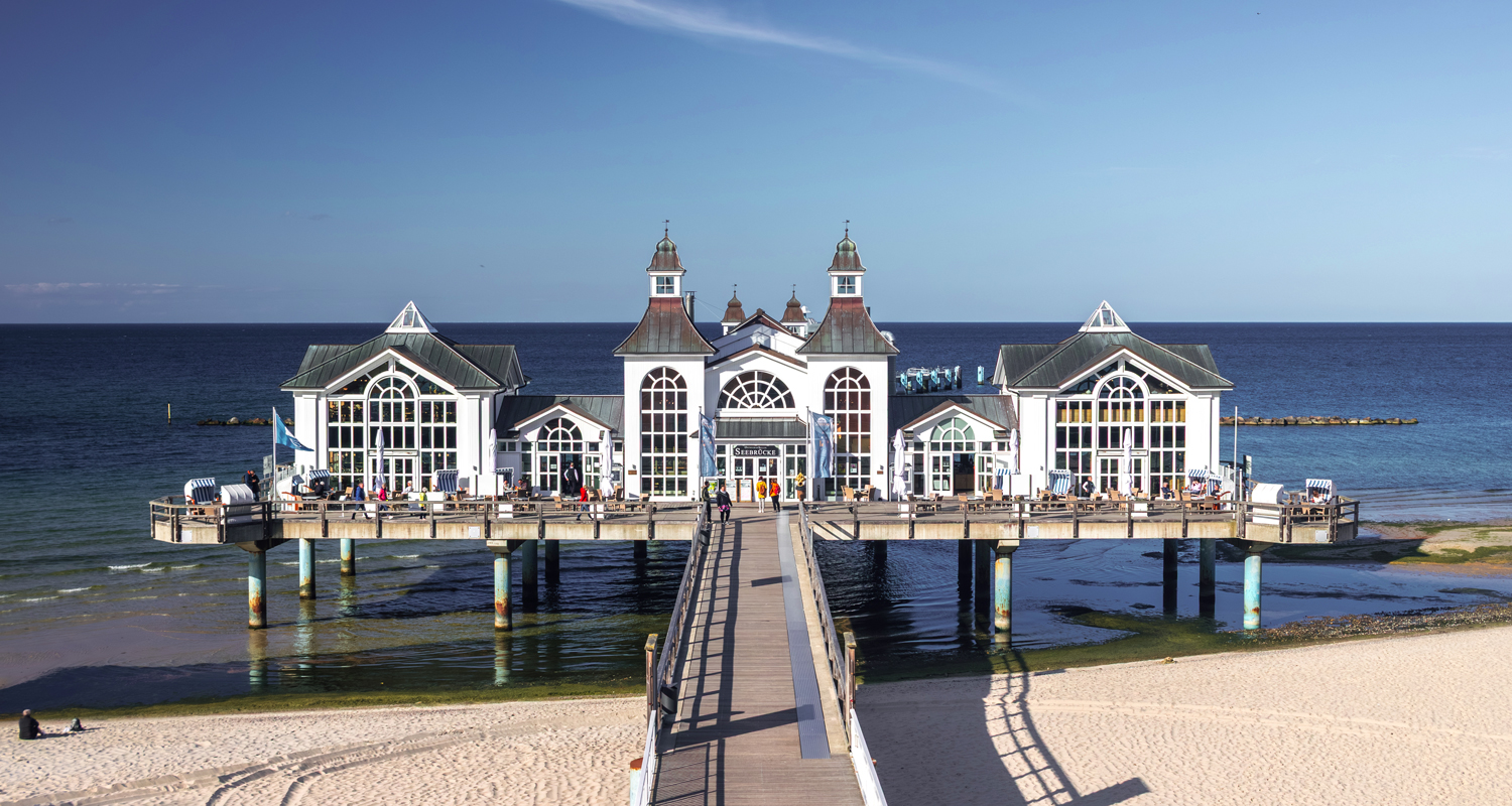 Frontalansicht des ikonischen weißen Seebrückengebäudes von Sellin, das sich über das klare, blaue Wasser der Ostsee vor der Insel Rügen (Deutschland) erstreckt.