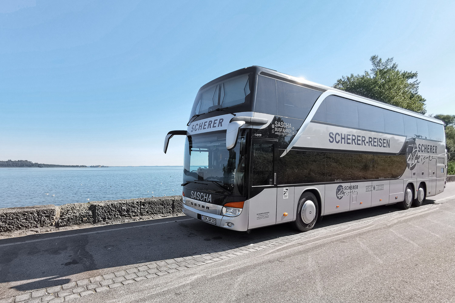Saschas silberner Doppeldeckerbus direkt am Meer bei blauem Himmel.