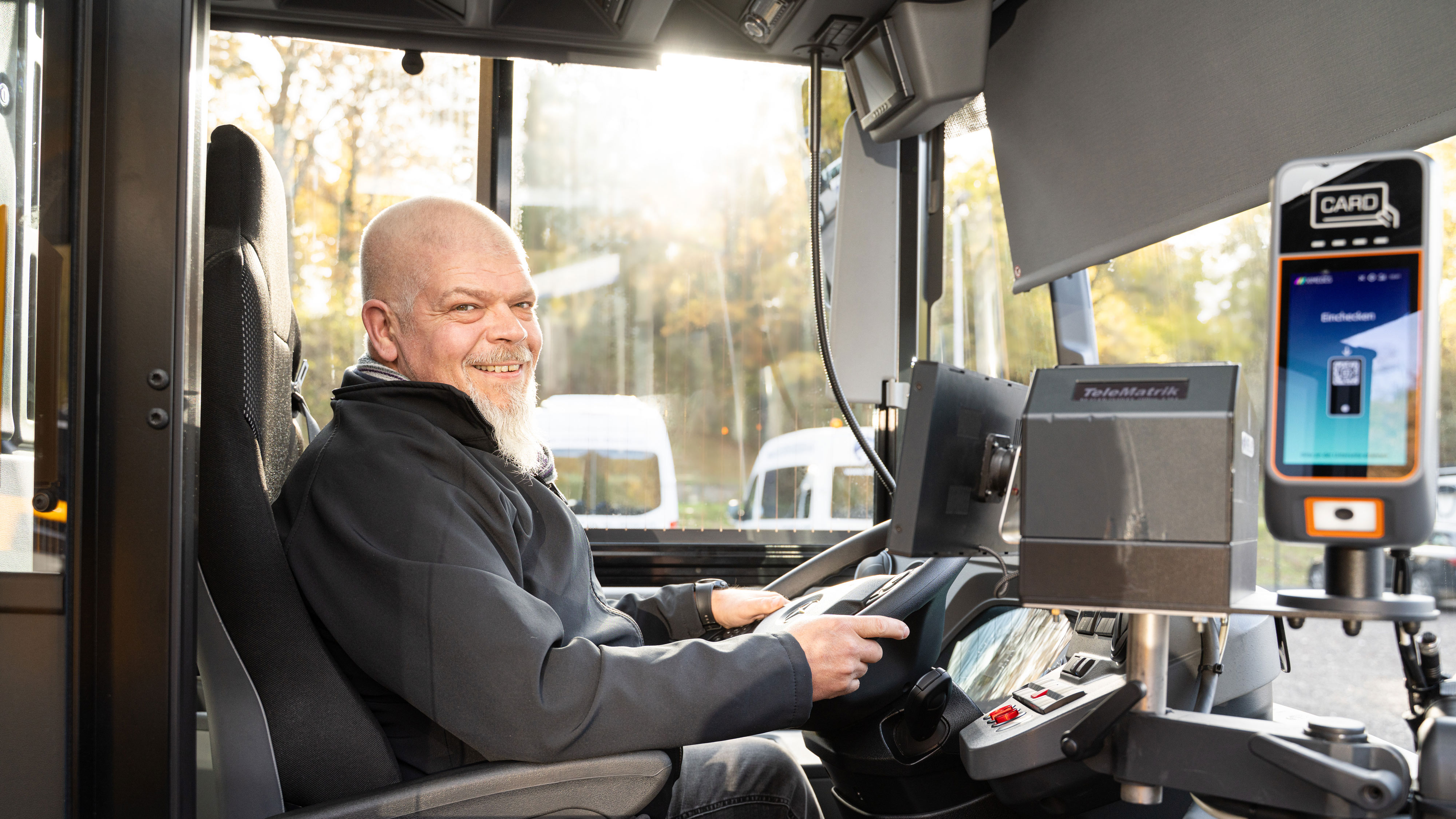 Scherer-Reisen Busfahrer sitzt am Steuer, hält das Lenkrad und lächelt in die Kamera.